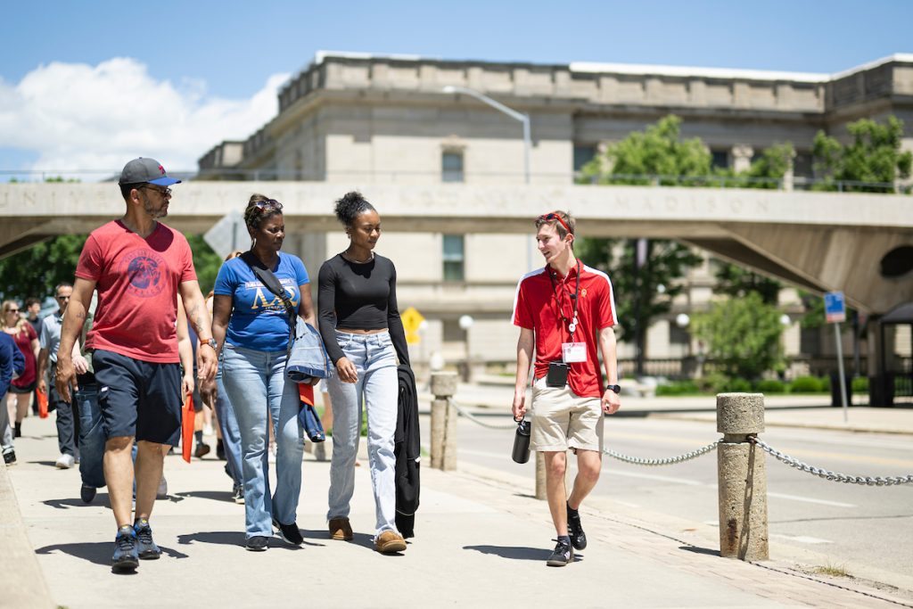 Students and families walking campus on a sunny day led by a campus tour guide in a red shirt.