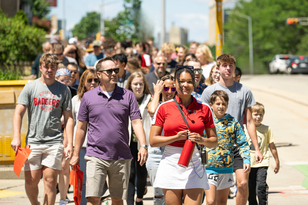 A group of people walk together along a sunny outdoor path, led by a student campus tour guide.