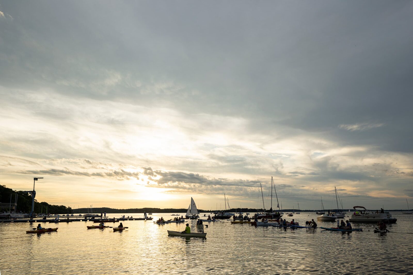 Sailboats and paddle boards on Lake Mendota during sunset.