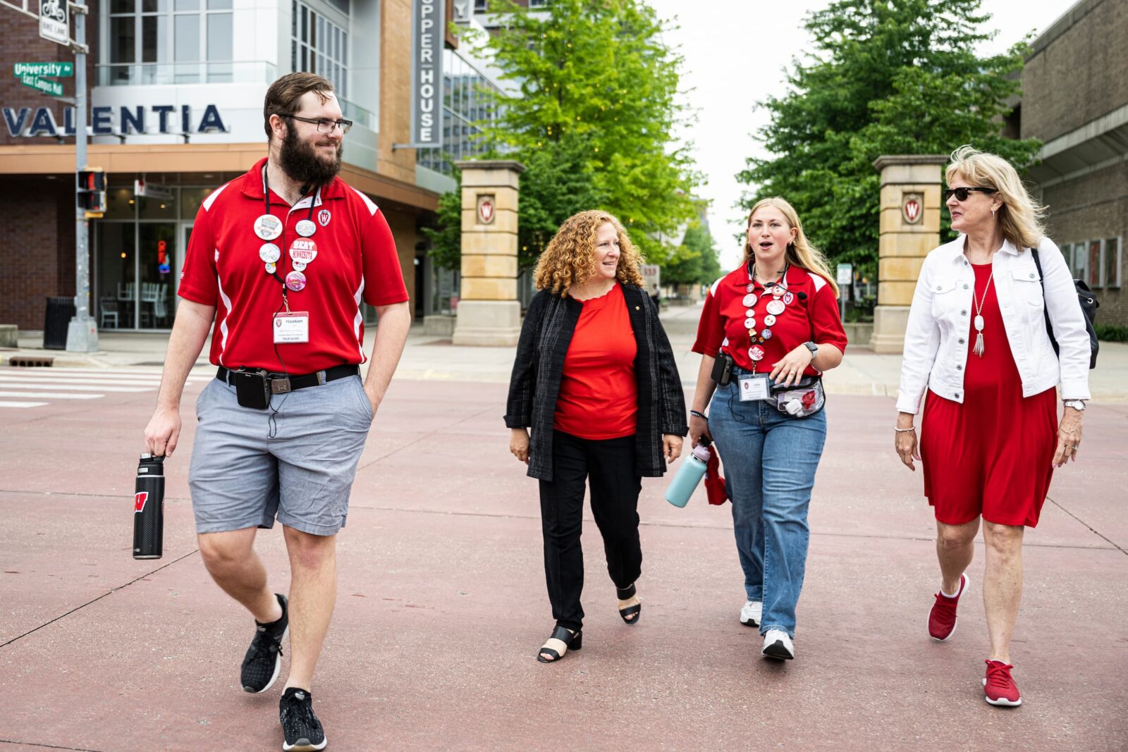 Four people walk together along a tree‑lined campus path, including two student guides, the UW chancellor, and vice chancellor for student affairs.